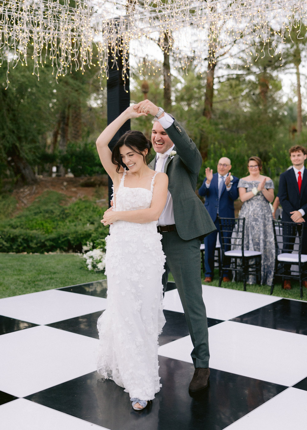 Bride twirling under her groom's arm on a black-and-white dance floor beneath hanging lights